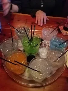 Overhead: tray of colorful drinks with ice, hands on dark bar.