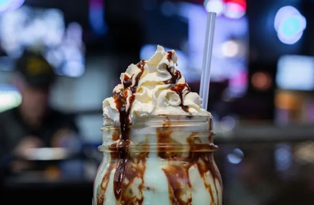 Milkshake in mason jar with whipped cream and dripping chocolate syrup.