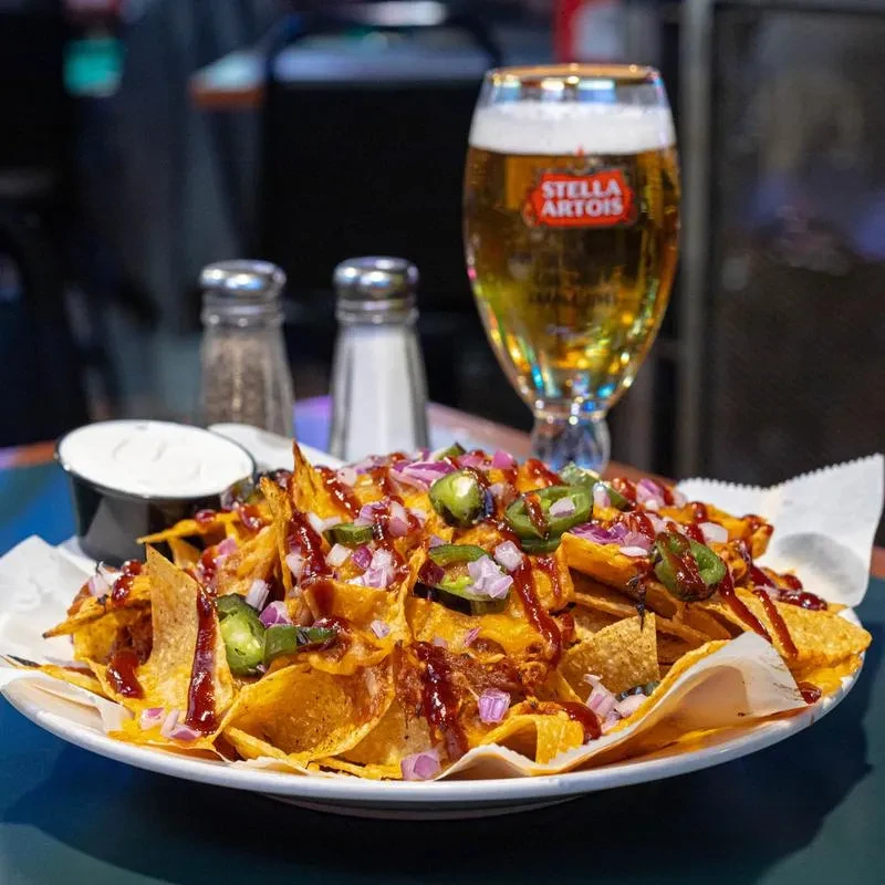 Loaded nachos with BBQ sauce, sour cream, and a Stella Artois beer.