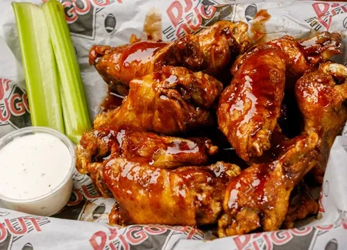 Basket of glossy barbecue chicken wings with celery and creamy dip.