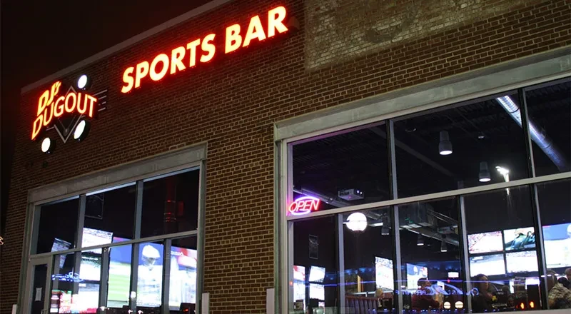 Bright neon signs illuminate DP Dugout Sports Bar's brick facade at night.