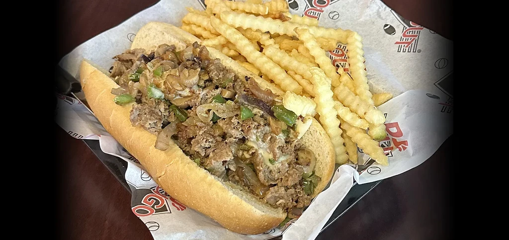 Cheesesteak with melted cheese, crinkle-cut fries, served on branded paper.