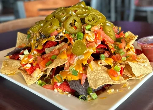 Overflowing nachos with melted cheese, jalapeños, diced tomatoes, green onions.