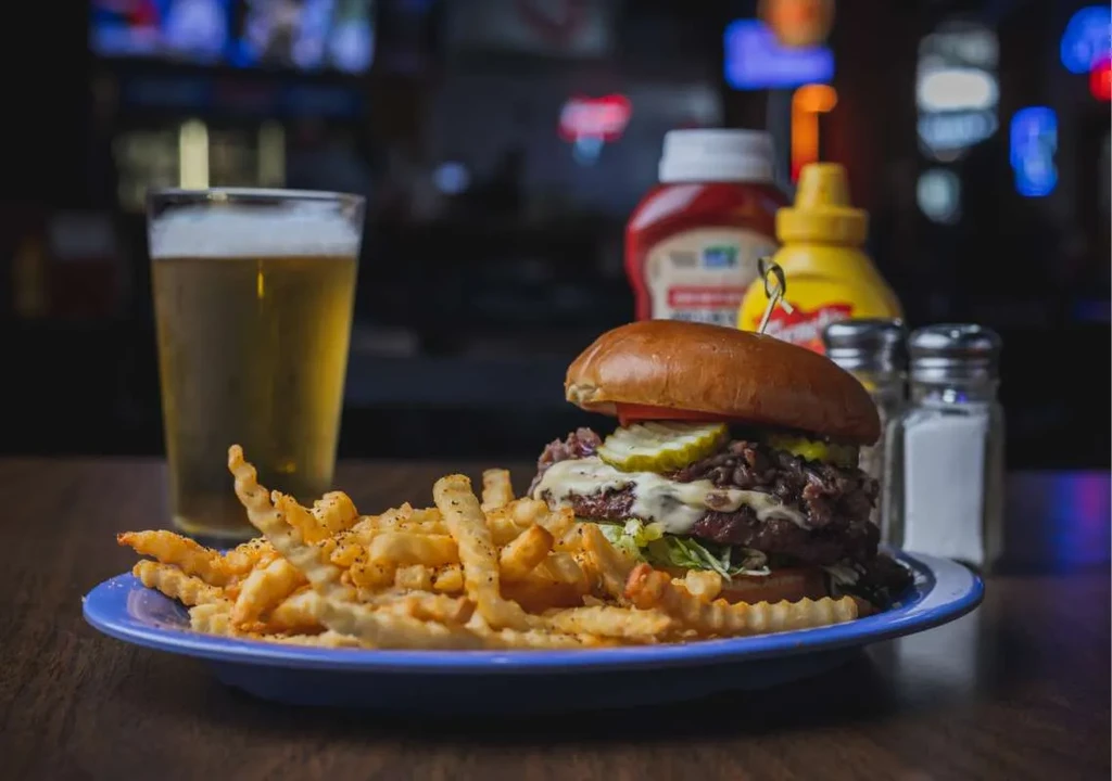 Large burger, crinkle fries, and beer on a dark wooden table.