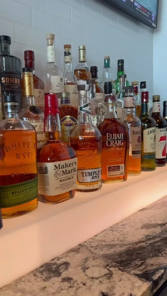 Well-stocked bar shelf displaying various whiskey and rye bottles.