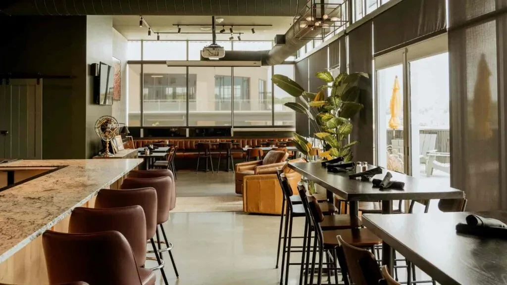Empty modern restaurant interior with bar, varied seating, and large windows.