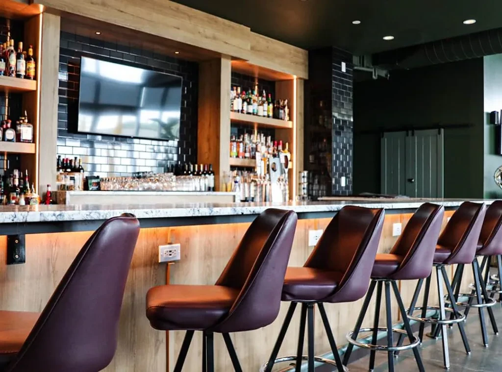 Empty modern bar: dark green walls, wooden counter, red leather stools.
