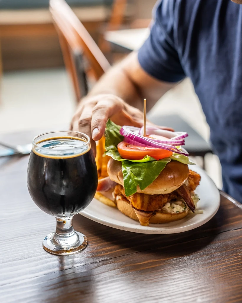 Fried chicken sandwich, dark beer, and a person's hand.