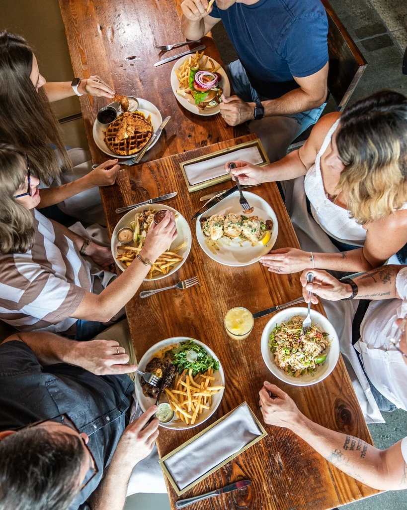 Six people dining at a rustic table laden with diverse dishes.