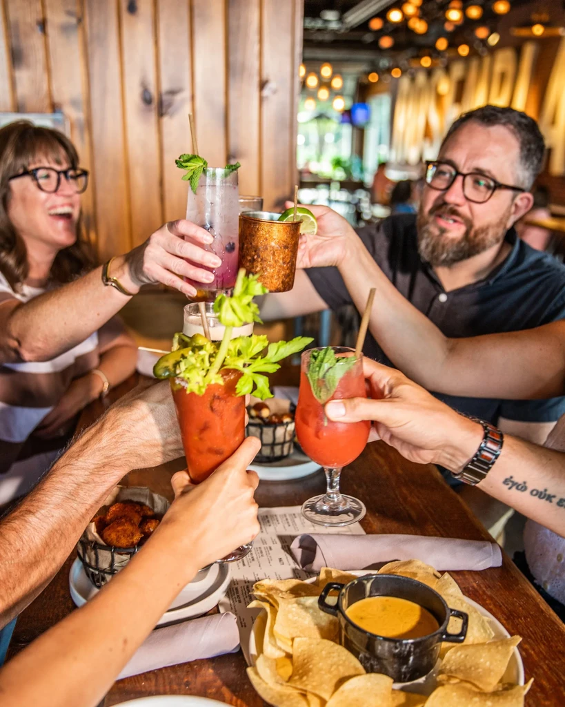 Group toasting with colorful cocktails and appetizers at a restaurant.