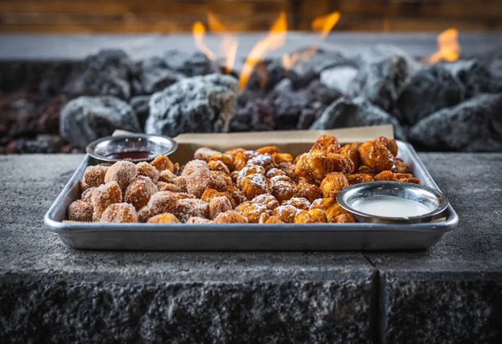 Tray with powdered and glazed snacks, red and white dips, by fire.