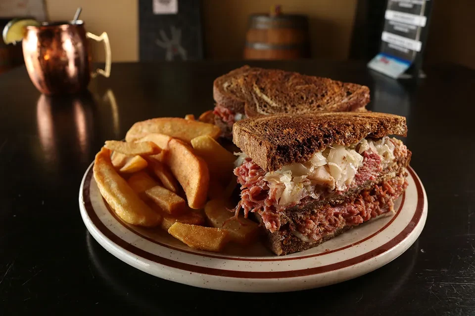 Reuben sandwich and fries with a copper mug in a dim restaurant.