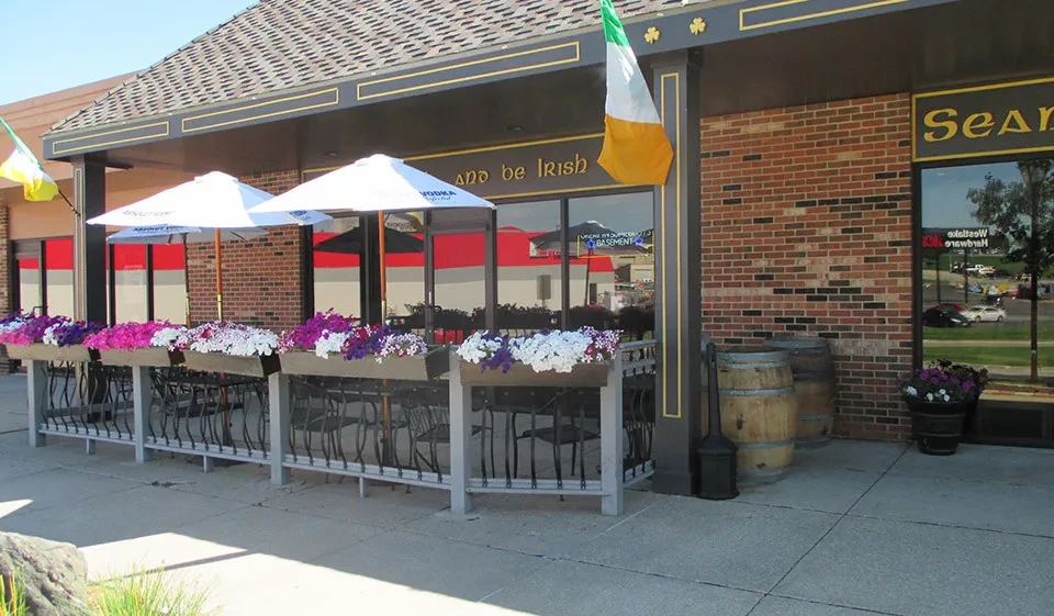 Irish-themed restaurant Sean's exterior with patio, flags, flowers, and umbrellas.