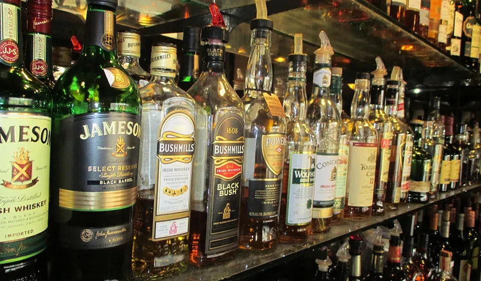 Well-stocked bar shelf with numerous whiskey bottles and pour spouts.