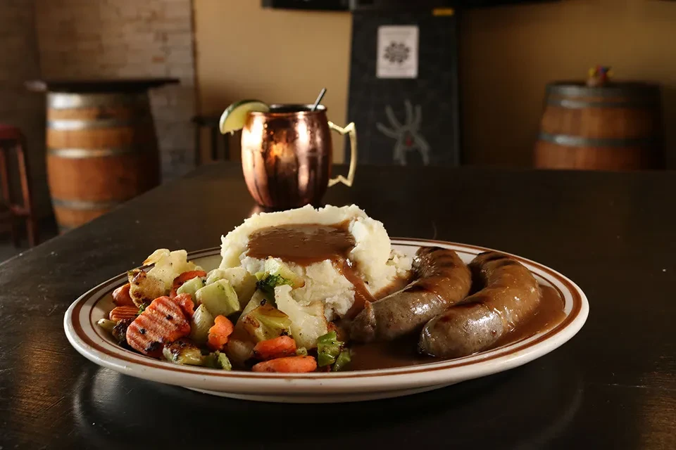 Grilled sausages, mashed potatoes, vegetables with gravy, and a copper Moscow Mule.