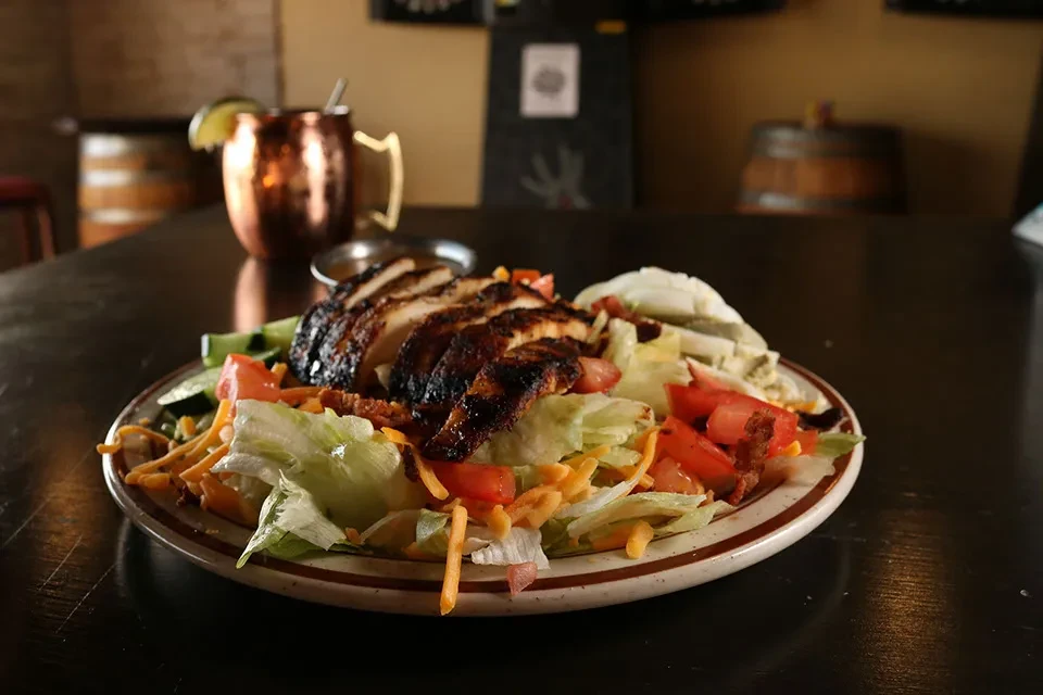 Close-up of a grilled chicken salad with a copper Moscow Mule.