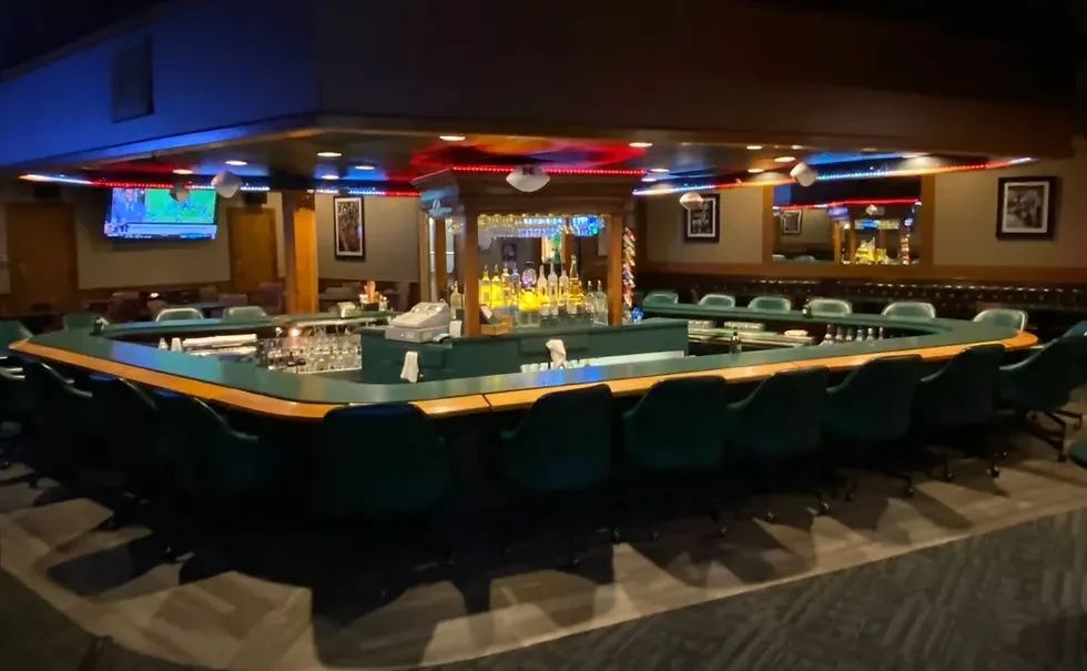 U-shaped bar with green stools, bright liquor display, and red-blue LED lights.