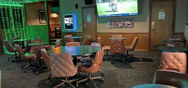 Dim bar game room with tables, chairs, TV, and dartboard.