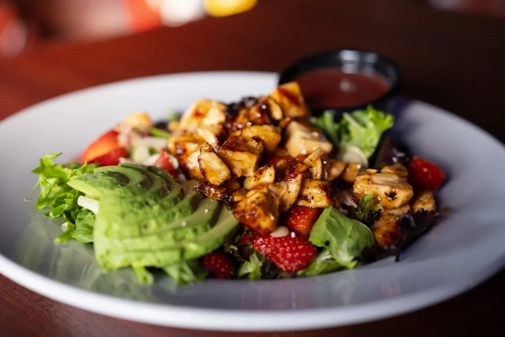 Vibrant mixed greens salad with glazed chicken, avocado, strawberries.