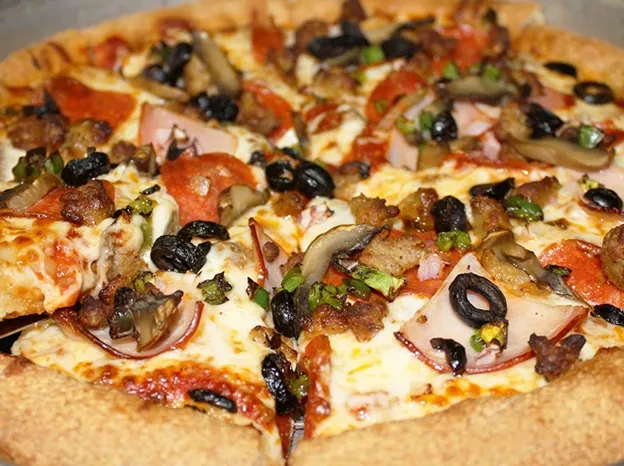 Close-up of supreme pizza with pepperoni, olives, peppers, one slice pulled.