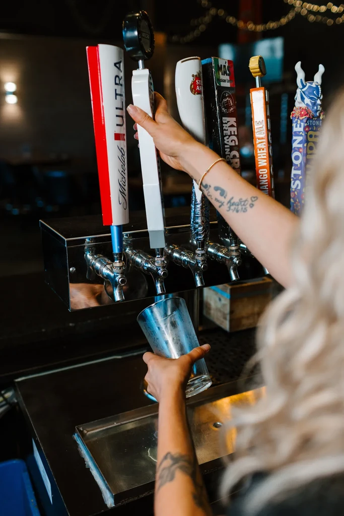A bartender's hands pour beer from a tap, brands visible.