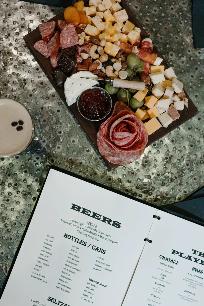 Charcuterie board, cocktail, and open menu on a textured table.