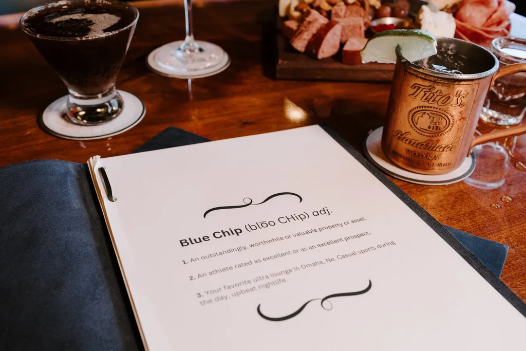 Bar table with 'Blue Chip' menu, two cocktails, and charcuterie.