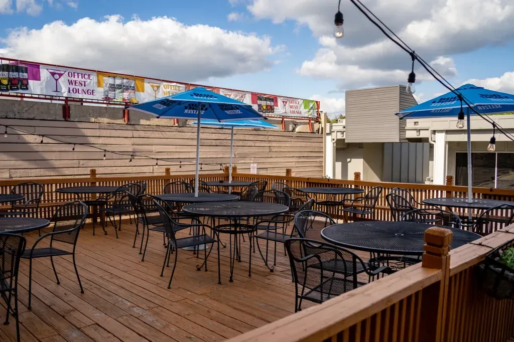 Empty outdoor patio with black tables, blue umbrellas, and string lights.