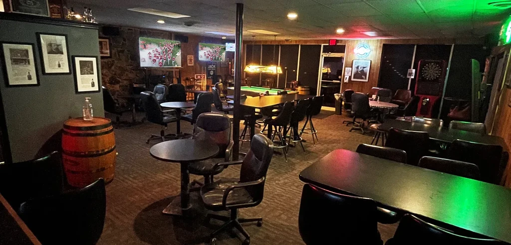 Empty, dimly lit sports bar interior with seating, pool table, and TVs.