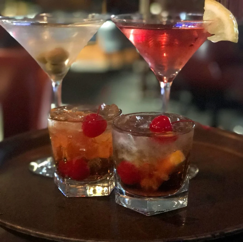 Four alcoholic cocktails with garnishes on a dark tray.