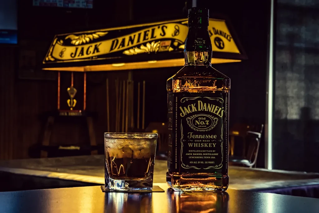 Jack Daniel's bottle, whiskey glass, and lighted sign in bar.