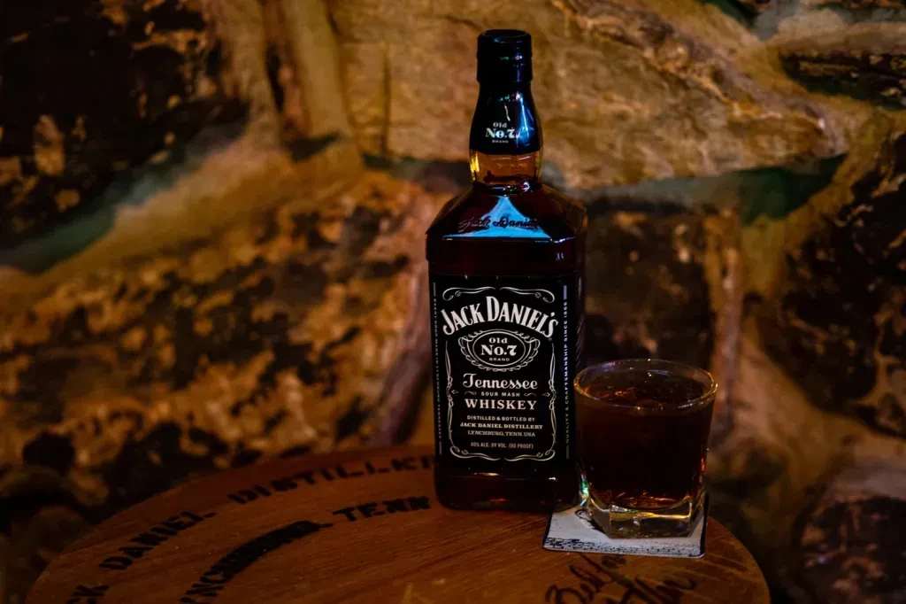 Bottle of Jack Daniel's whiskey and glass with ice on a barrel.
