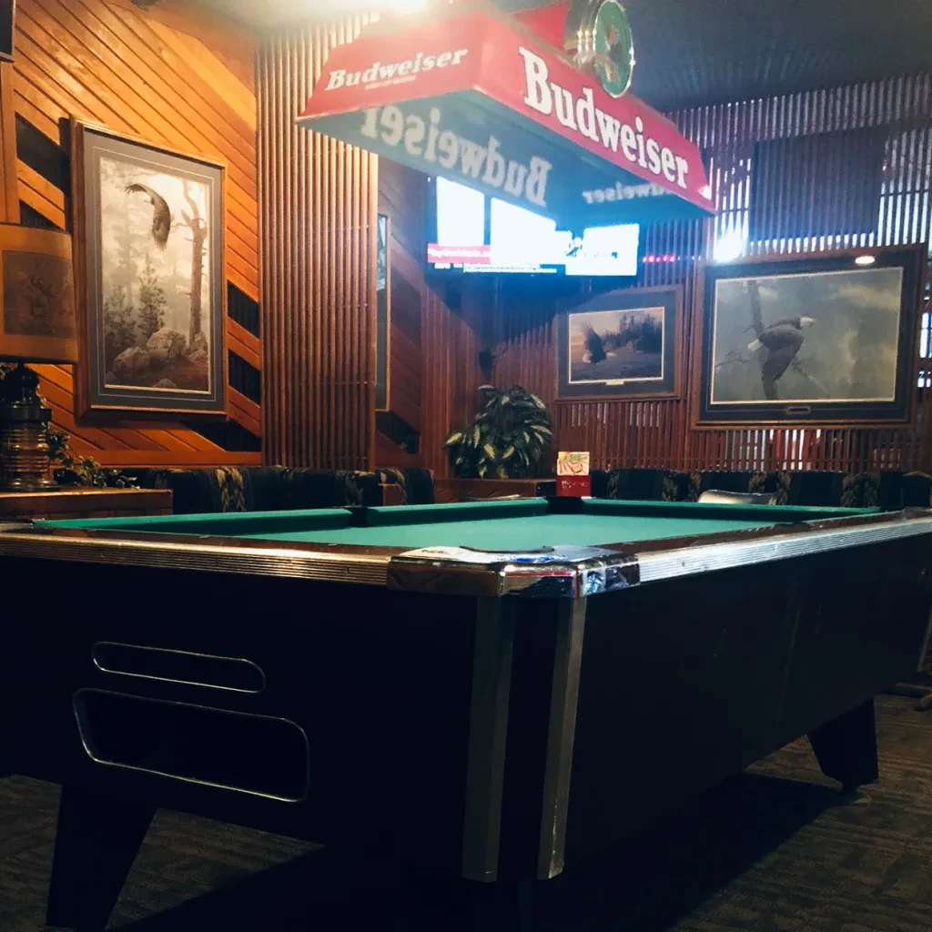 Rustic bar interior with a green pool table and Budweiser light.
