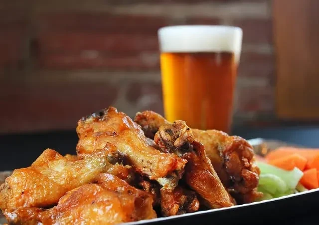 Close-up of crispy chicken wings, celery, carrots, and beer.