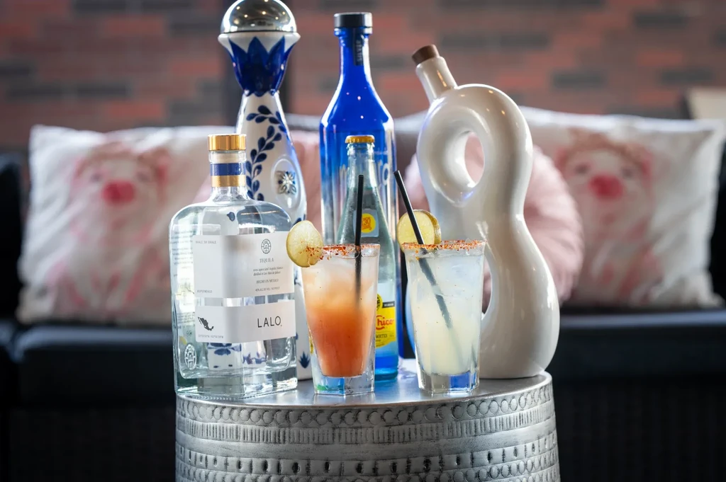 Two garnished cocktails and various liquor bottles on a metallic table.