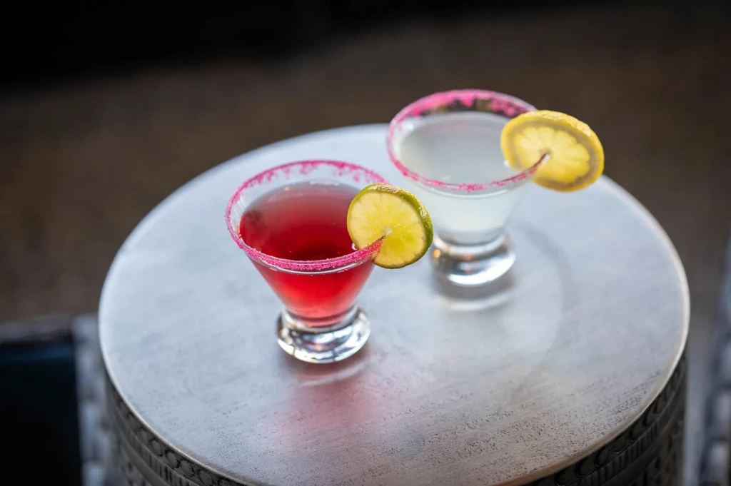 Two cocktails in martini glasses with sugared rims and citrus garnishes.