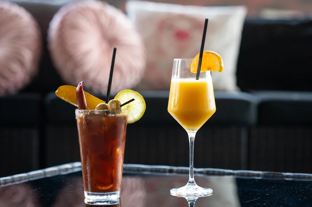 Dark red and orange garnished cocktails on a reflective bar.