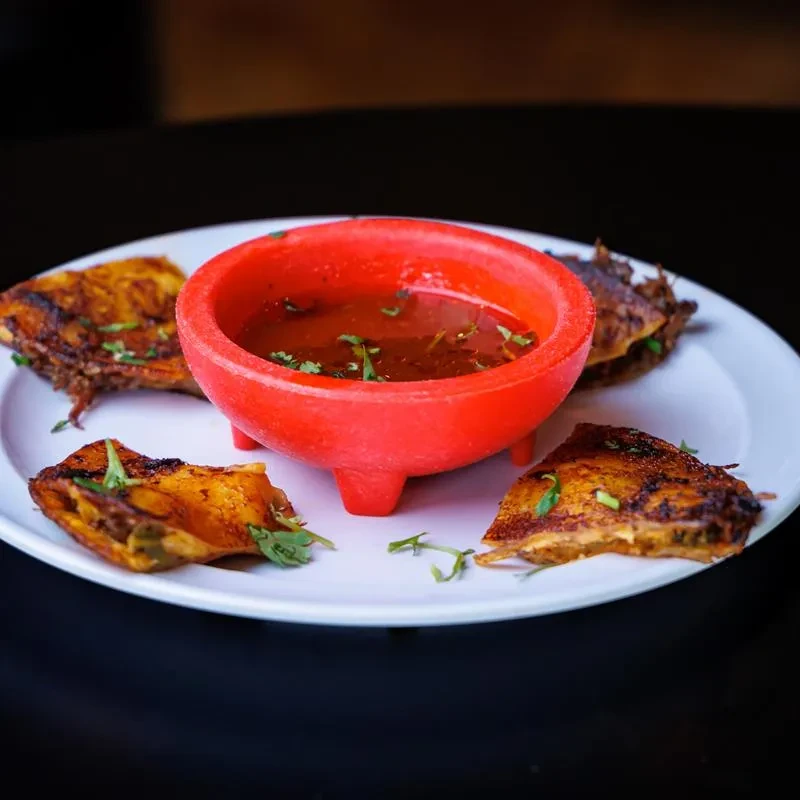 Grilled meat surrounds a garnished red molcajete of sauce.