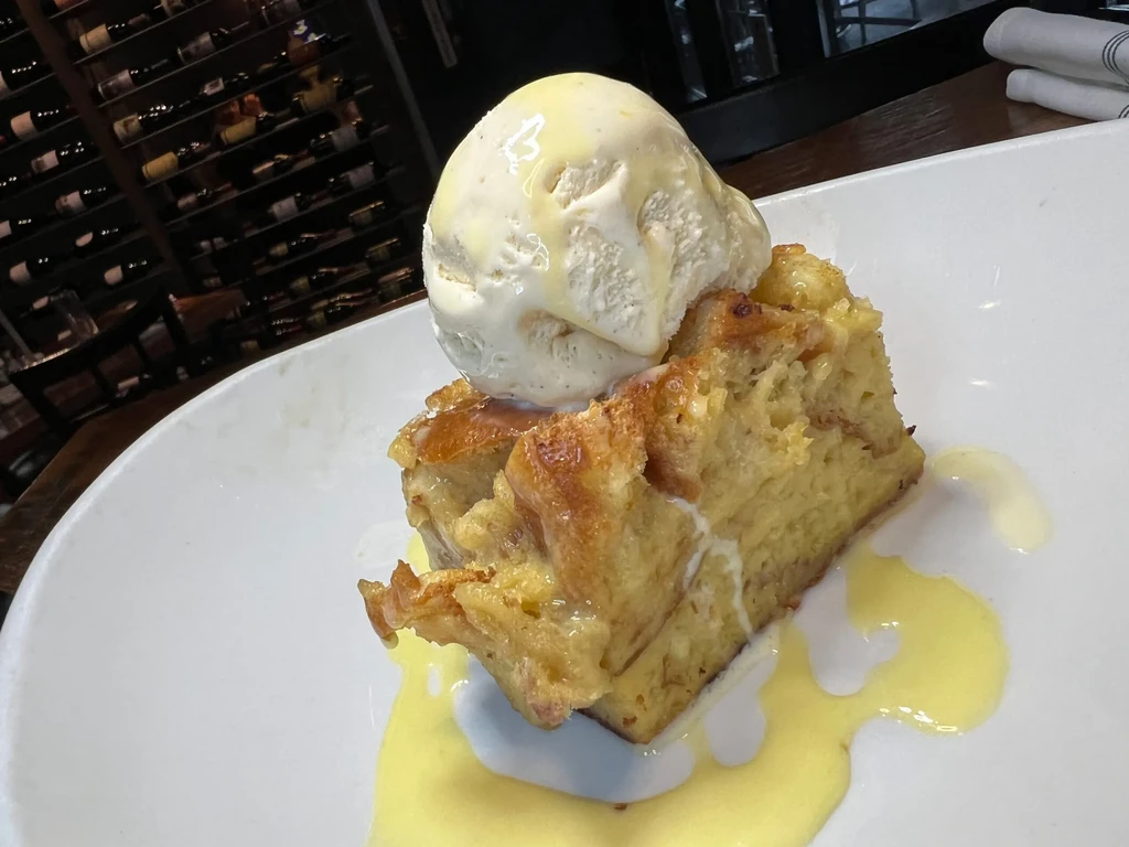 Golden brown bread pudding, melting vanilla ice cream, creamy sauce on a plate.