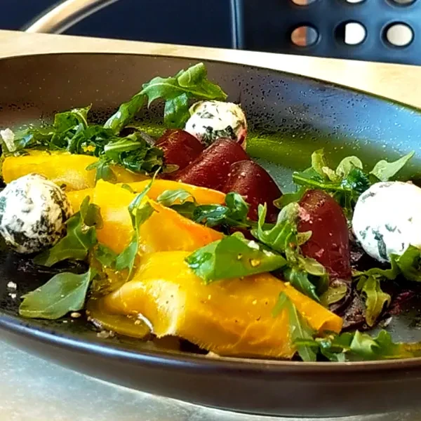 Close-up of colorful beet salad with arugula and cheese on dark plate.