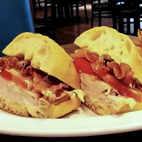 Rustic sandwich cut in half, revealing meat, bacon, tomato, and sauce.