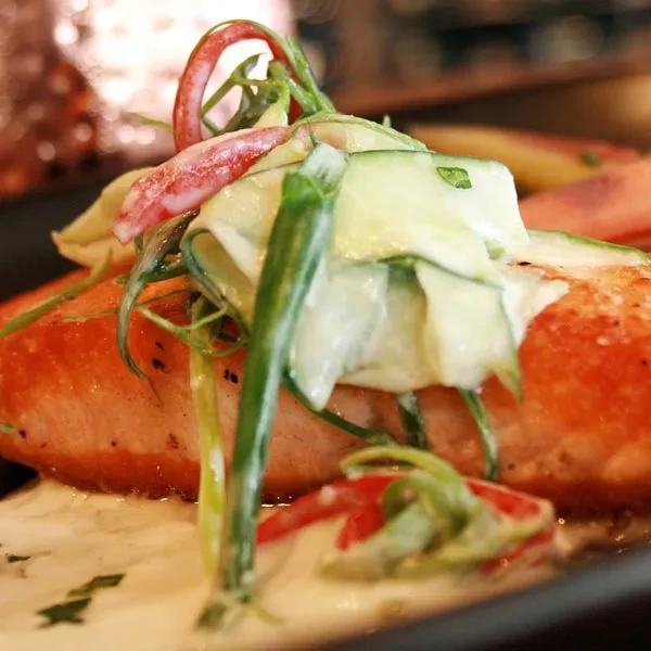 Seared salmon on creamy sauce, topped with green and red garnishes.