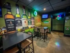 Jameson-themed bar interior with bottle cutouts, neon signs, and high-top tables.