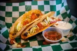 Two hard-shell tacos with meat, lettuce, tomatoes, creamy sauce, and salsa.
