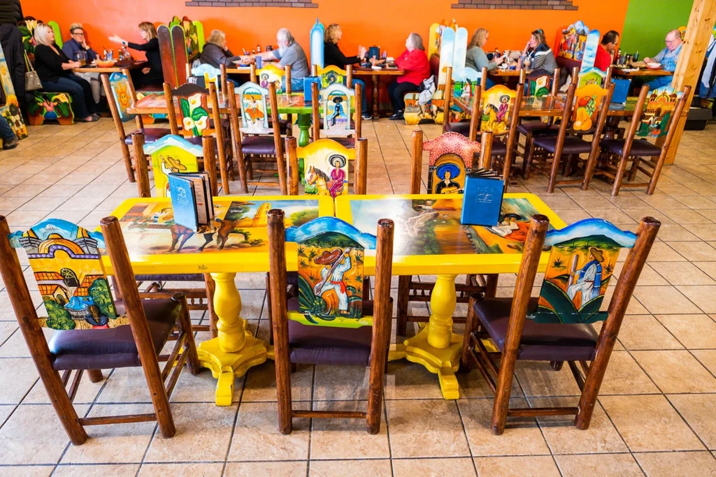 Vibrant restaurant interior with hand-painted folk art furniture, colorful walls, and diners.