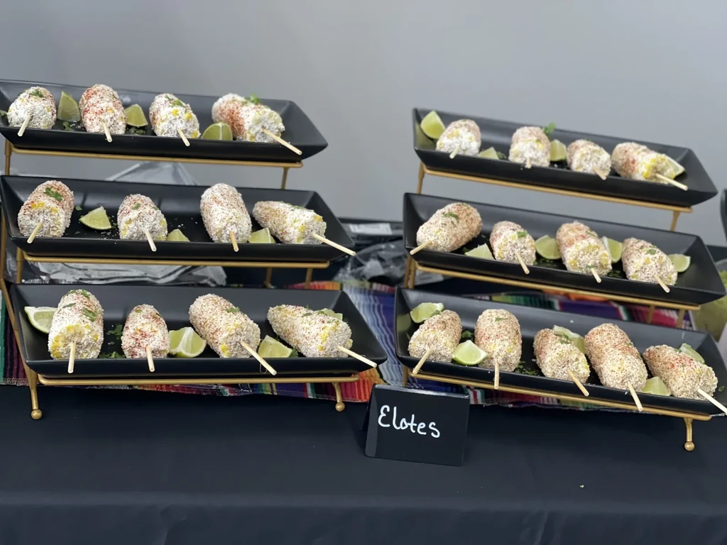 Garnished Mexican street corn (Elotes) on sticks, arranged on tiered stands.