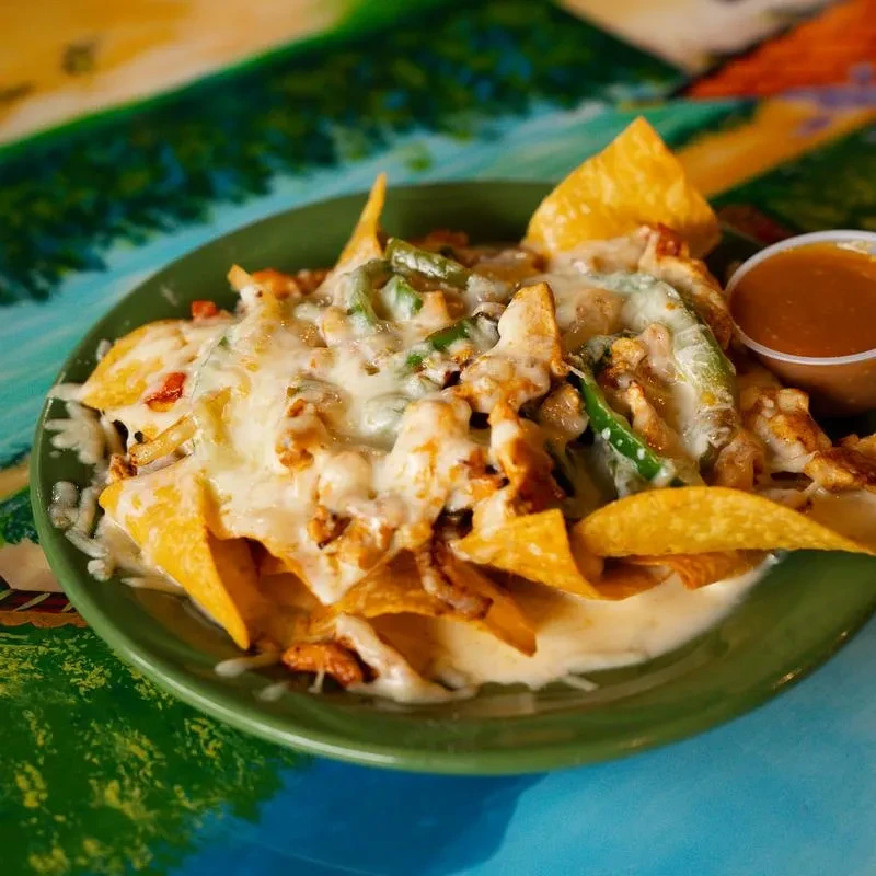 Plate of chicken nachos with melted cheese, jalapeños, and salsa.