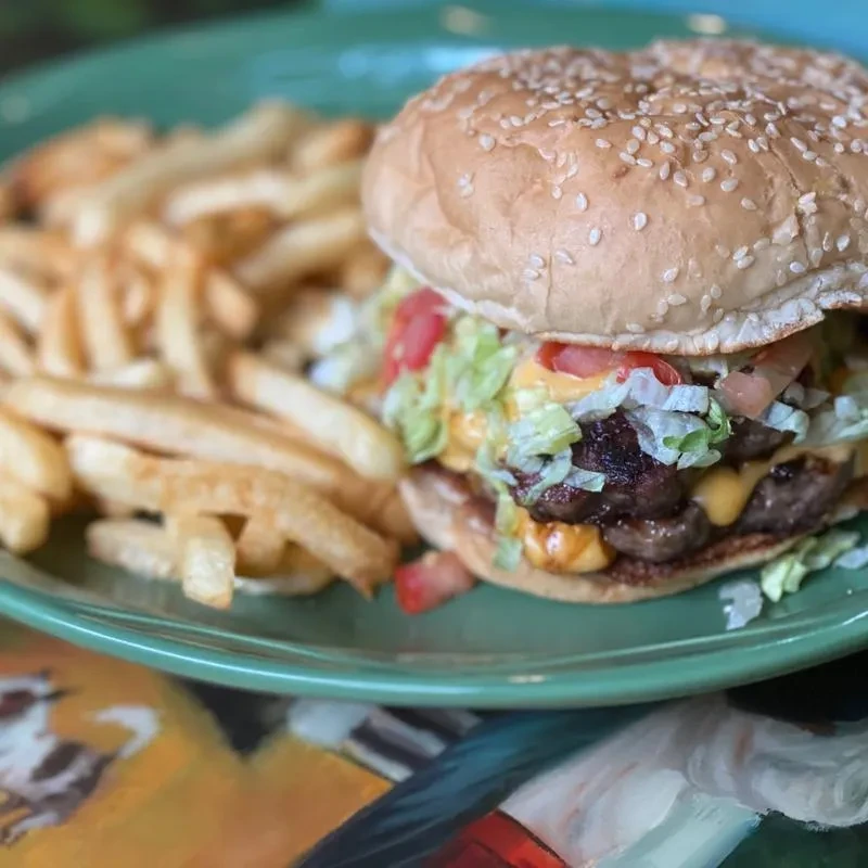 Close-up of a double cheeseburger and fries on a green plate.
