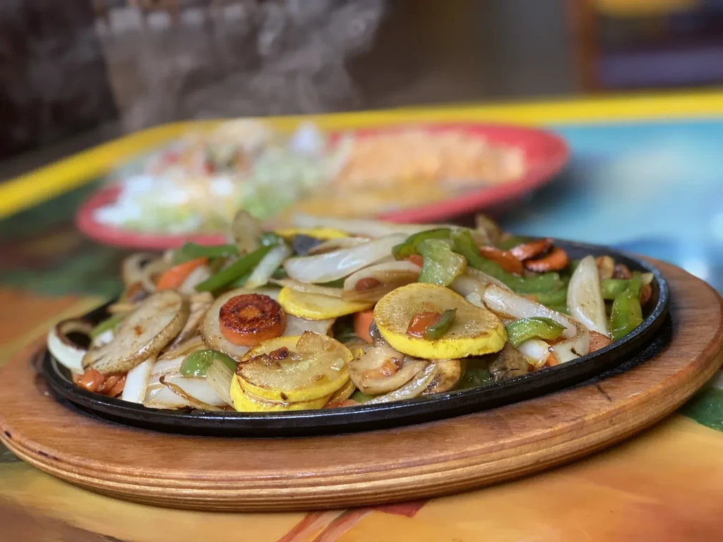 Colorful, sizzling sautéed vegetables in a black cast-iron dish.