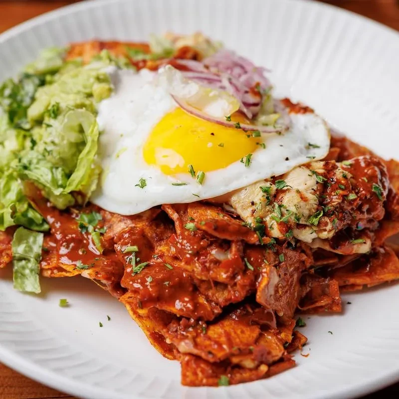 Colorful chilaquiles dish with a fried egg, guacamole, and shredded chicken.